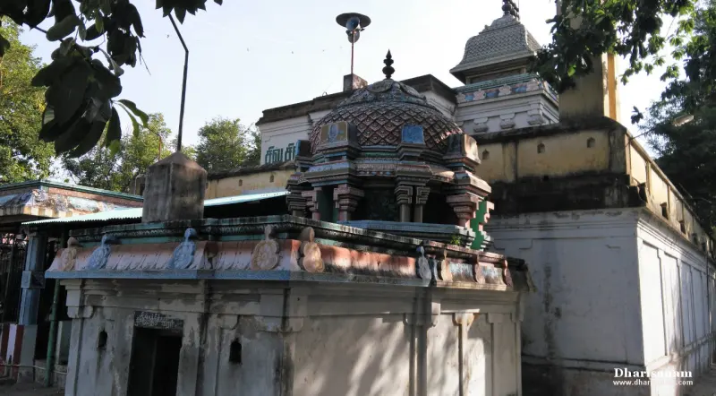 A small shrine with a patterned dome in front of a white temple wall and a yellow-topped enclosure wall