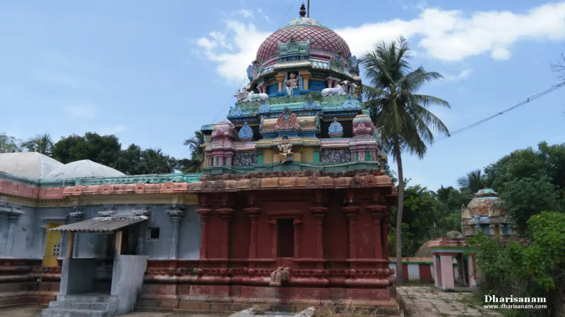 The coloured tower above a red stone base, with a small shrine at the lower right and palms behind