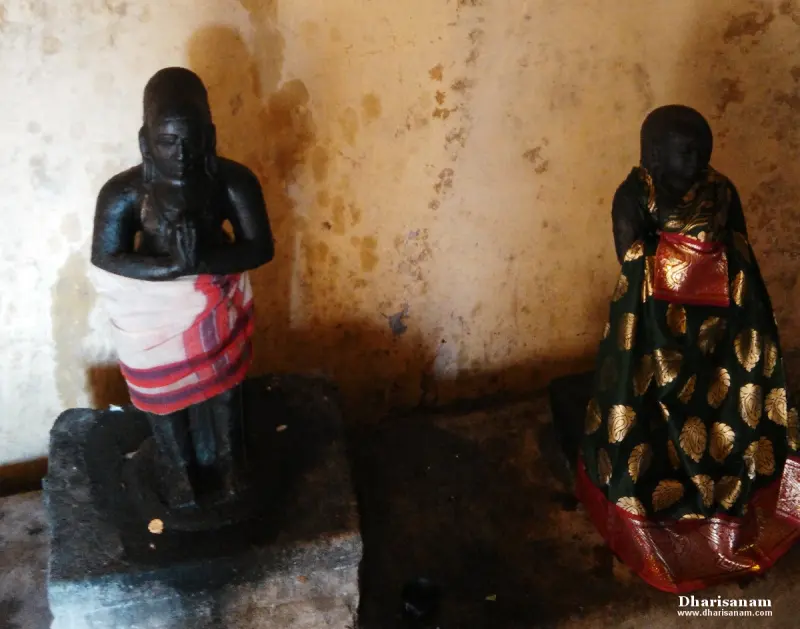 A dark stone idol with joined hands in a striped cloth beside another dressed in dark gold-patterned silk