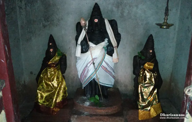 Three black stone idols, the tall middle one in white and the two on the sides in gold cloth, with a hanging lamp