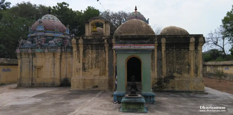 Domed stone shrines and a green shrine with an open doorway across a bare paved courtyard