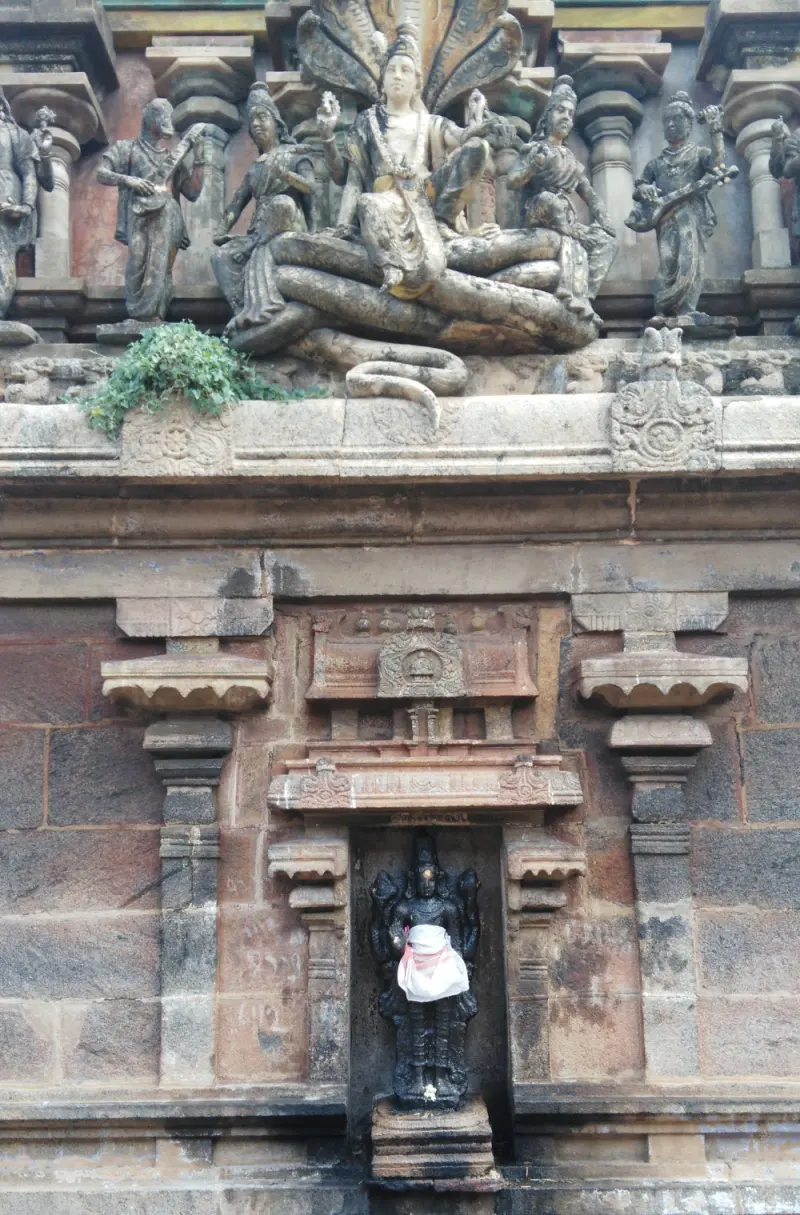 A dark stone figure with a white cloth stands in a wall niche; above it a figure sits on a coiled serpent.