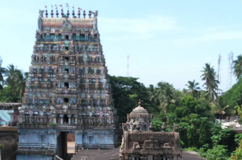 A tall tiered tower with painted figures, and the carved roof of a small shrine in front