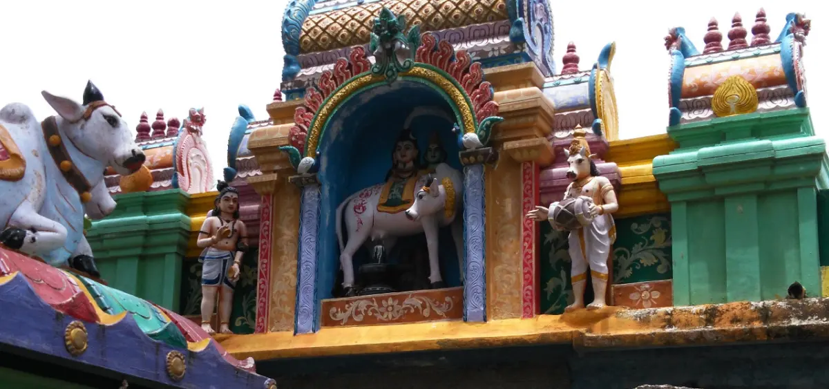 A colourful temple wall niche holding painted figures seated on a white bull, a Nandi and small figures at the sides.