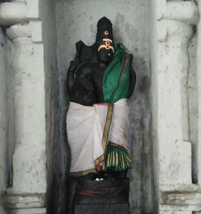 A black stone figure in a niche, dressed in a white cloth and a green shawl.