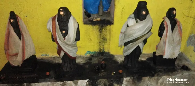 Four dark stone idols in white and orange cloths standing in a row against a yellow wall