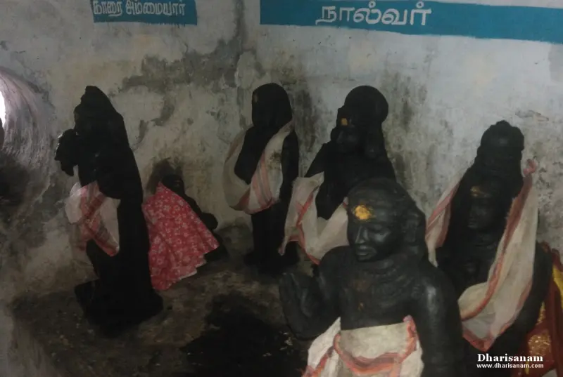 Group of black stone idols in a dim corridor, with a Tamil name board reading Nalvar