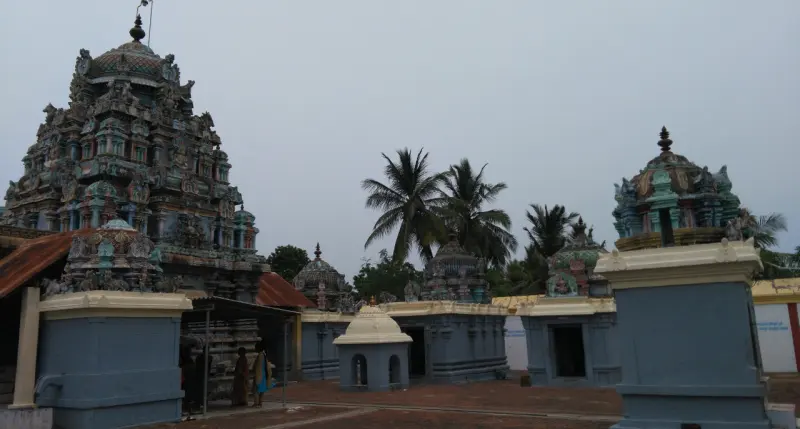 The tower at left, several domed shrines across a brick courtyard, and palms behind.