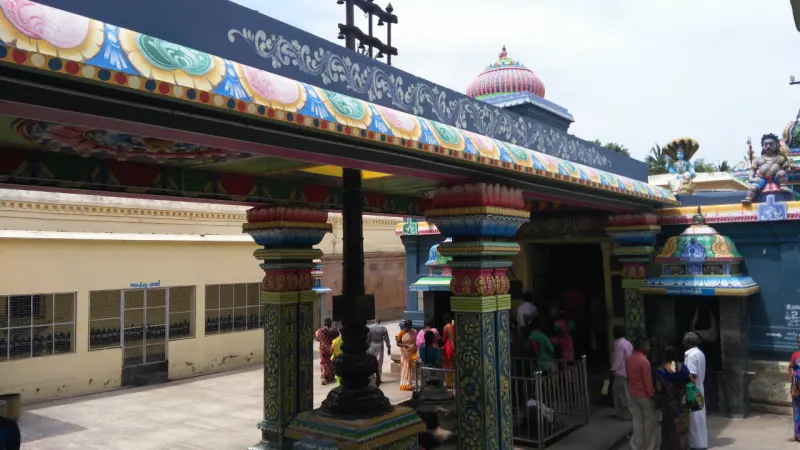 A painted pillared hall with a dark lamp post, devotees at the shrine doorway on the right