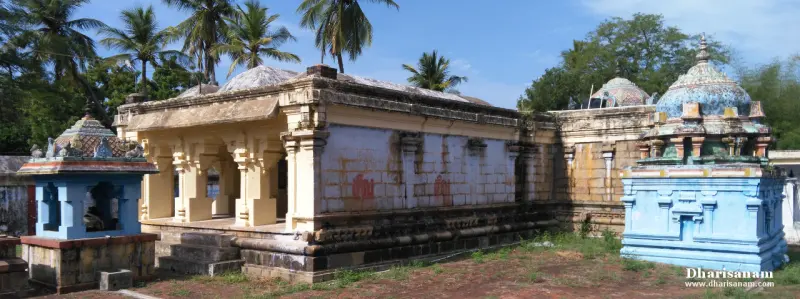 Yellow pillared hall flanked by two small blue shrines, with coconut palms behind