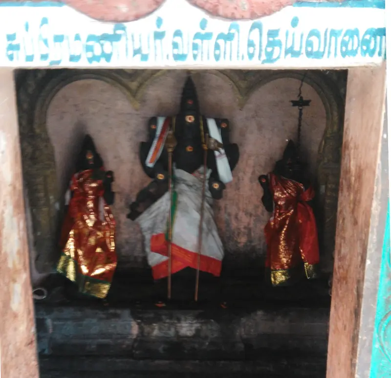 Three dark idols in a niche, a tall one with two staffs at the centre and a smaller figure in red on each side.