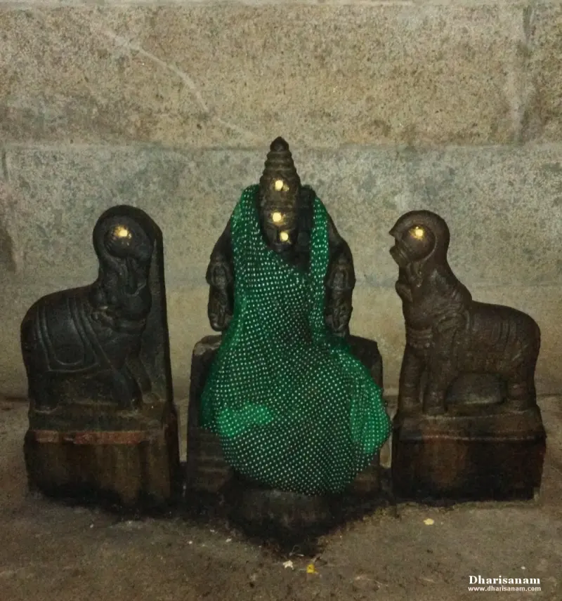 A small seated stone idol in a green dotted cloth with a carved animal figure on each side