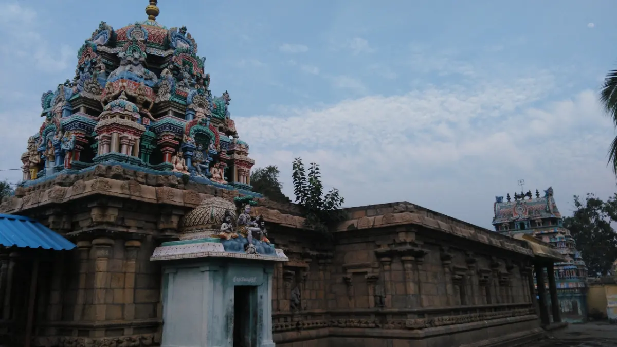 A stone temple wall with a painted sanctum tower rising above it, and another tower in the distance.