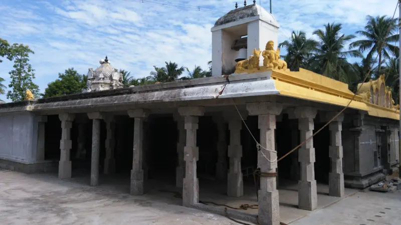 A long open hall with many square stone pillars and a flat roof edged in yellow, with small towers behind.