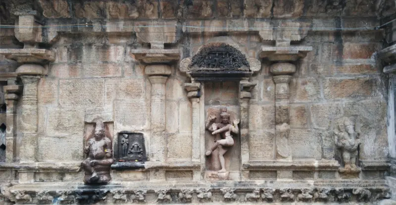 A stone wall with pilasters; a dancing figure stands in a central niche under an arch, with carved figures beside it.