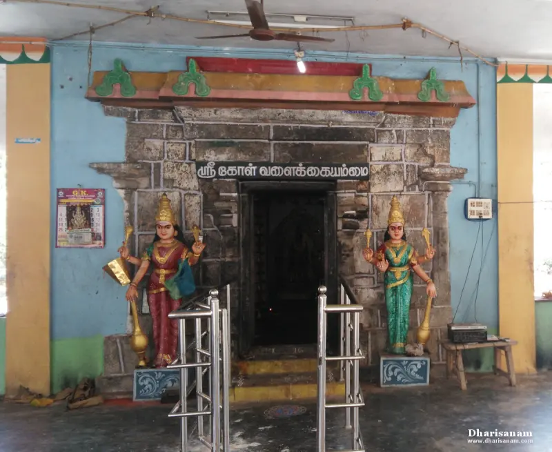 A stone sanctum doorway with a Tamil name board and a painted female guardian figure standing on each side