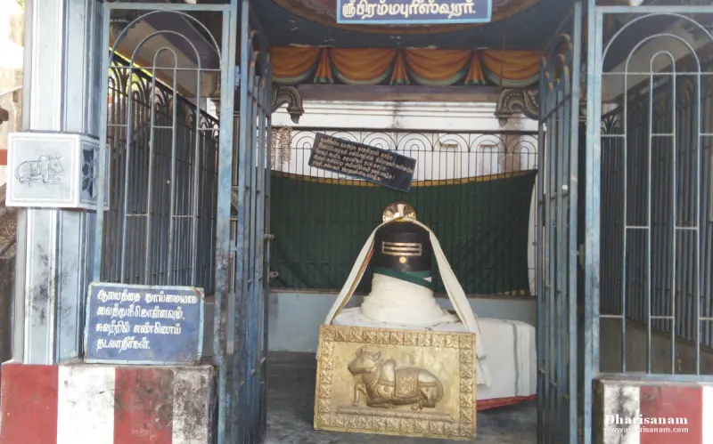 A black lingam draped in white cloth behind iron railings, with a brass plate of a bull in front