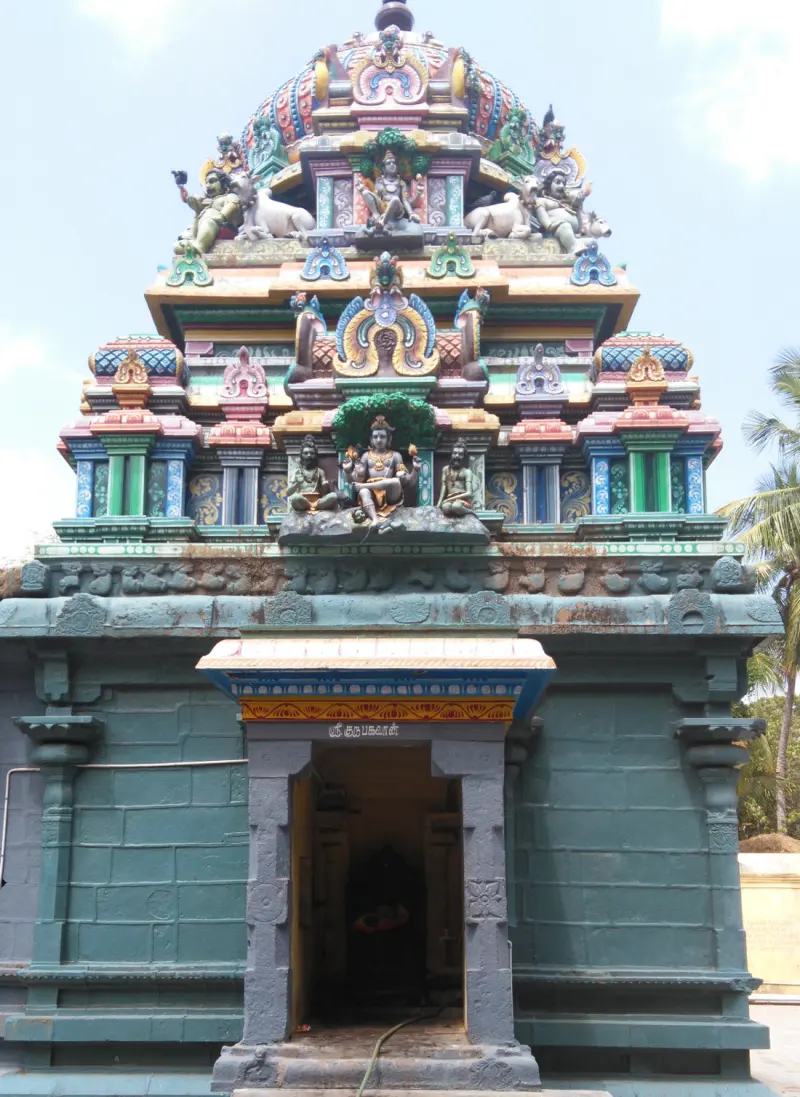 A stone doorway below a tiered vimana with many painted figures, under a pale blue sky