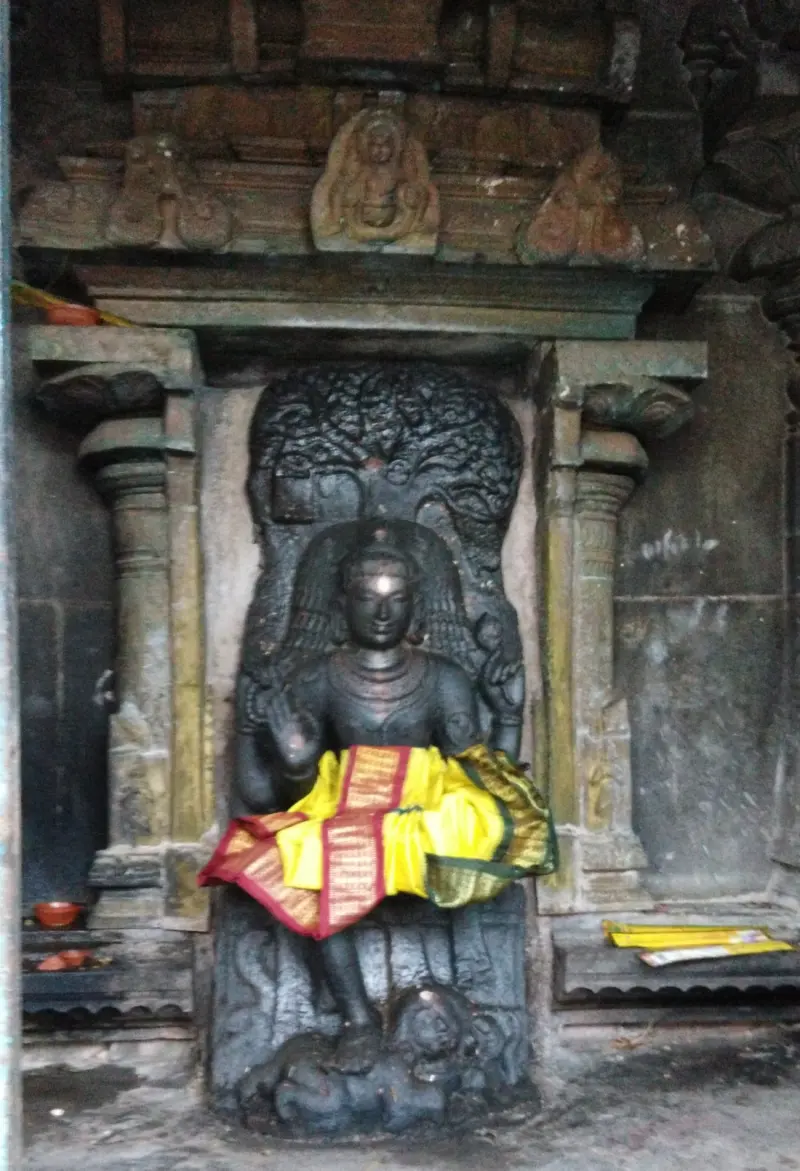 Seated dark stone figure in a niche, draped in yellow and red silk