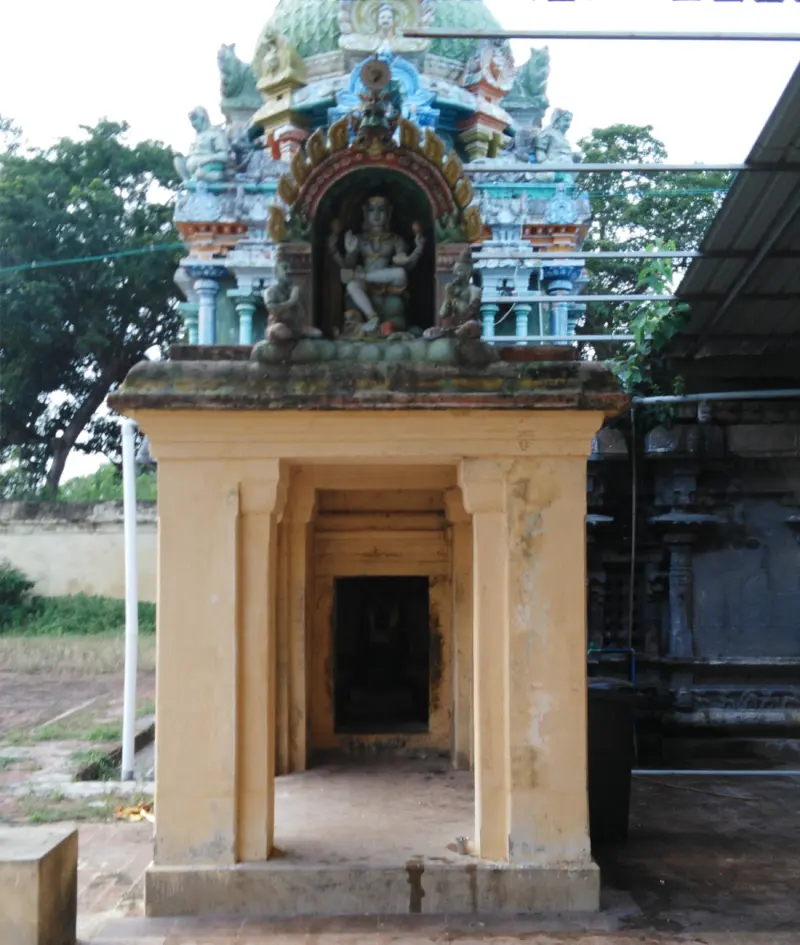A small pillared shrine with a seated four-armed figure in a niche above and a dark inner doorway.