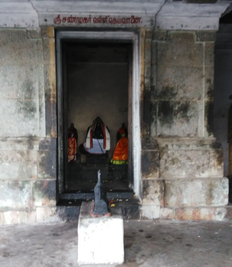 Doorway with a Tamil name board and three small figures inside, a spear before it