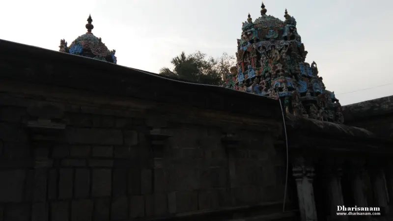 A dark stone wall in shade, with the sculpted tops of two towers showing above it