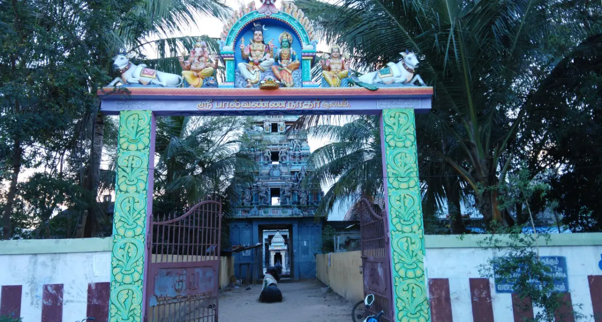 Painted entrance arch with a name board in Tamil and a tiered gopuram behind it