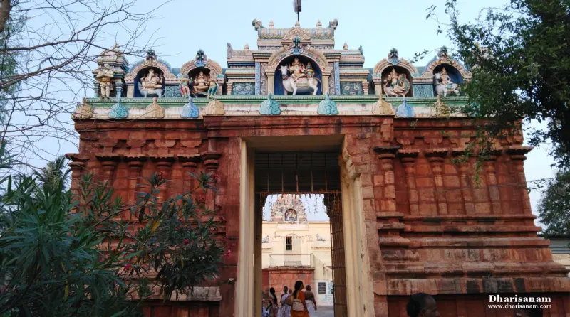 Red stone entrance tower topped with painted figures, with a second tower seen through the doorway