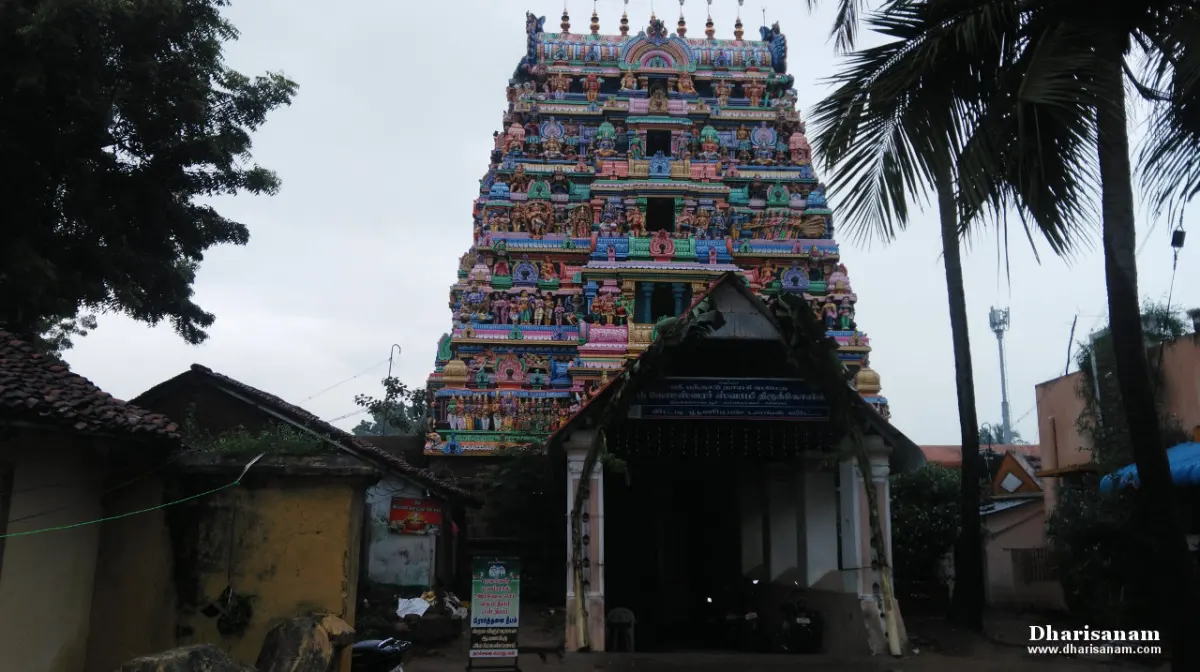 A colourful tiered gopuram behind a small entrance porch, with palm trees and houses around
