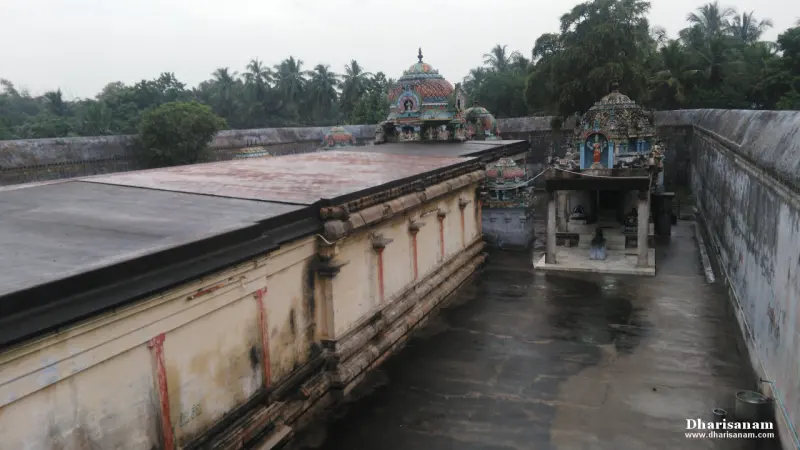View over a flat corridor roof to a paved passage with painted shrine roofs and palm trees beyond