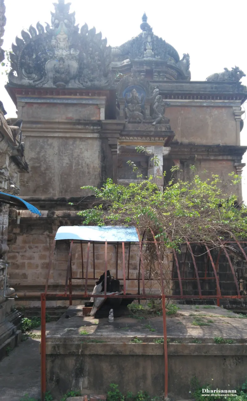 Layered tower with carved figures above a low stone platform covered by a rusty frame and creeper