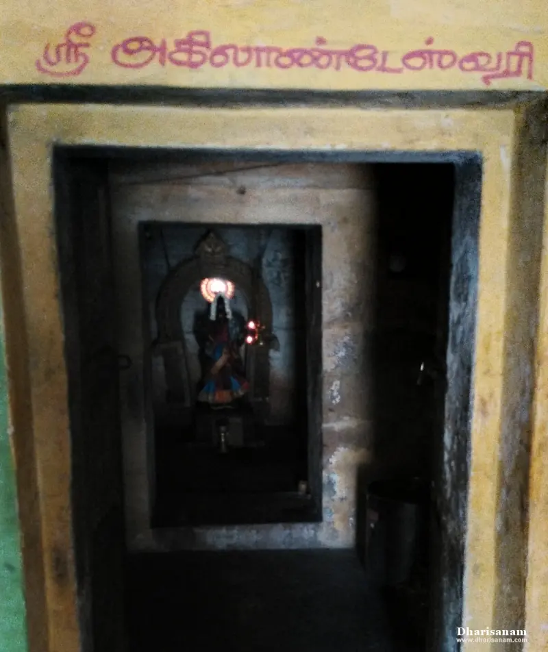 Dim shrine doorway under a red Tamil name board, with the Goddess lit by a lamp inside