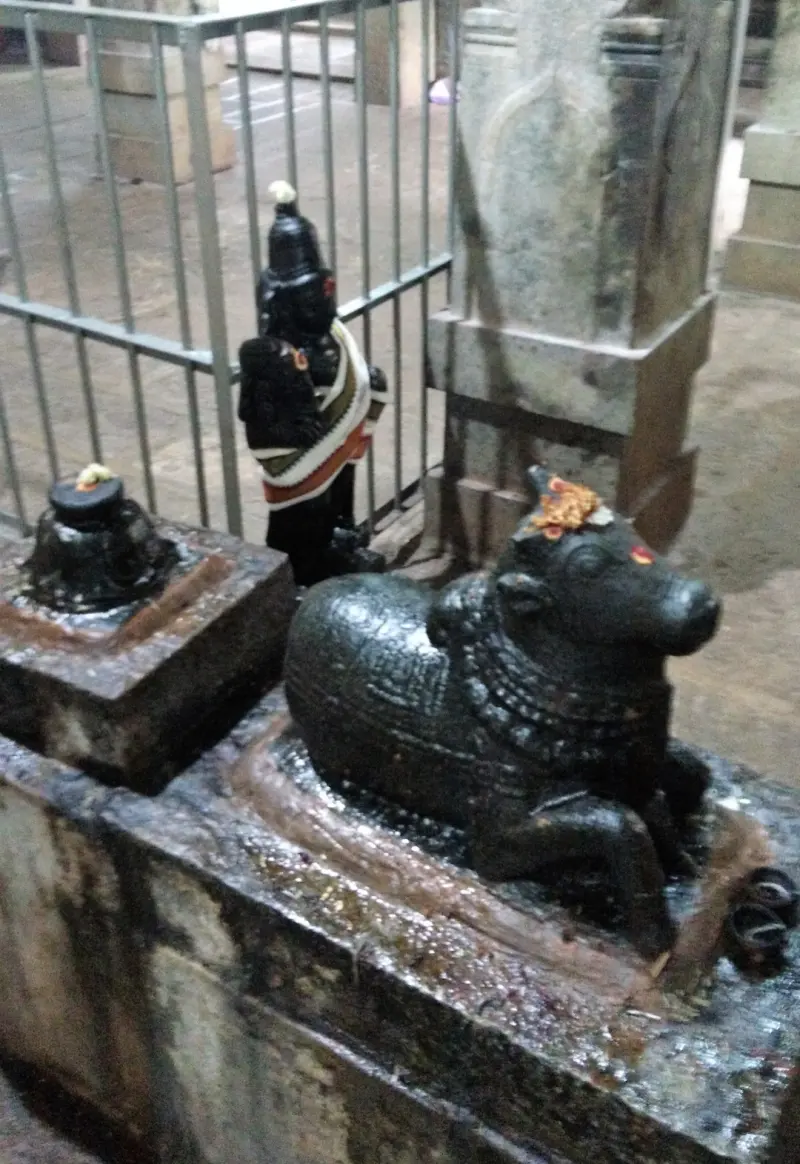 A black stone Nandhi lying down, with a small dark idol of a standing figure behind it and a lingam on the left.