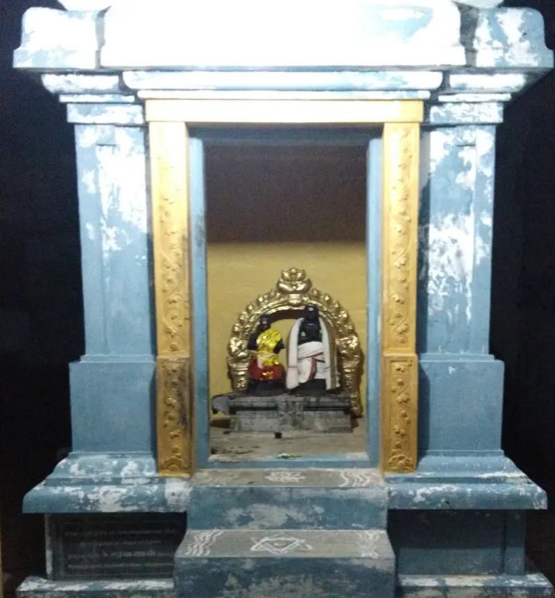 Two small dark idols under a gilded arch inside a blue shrine with gold-painted door posts.