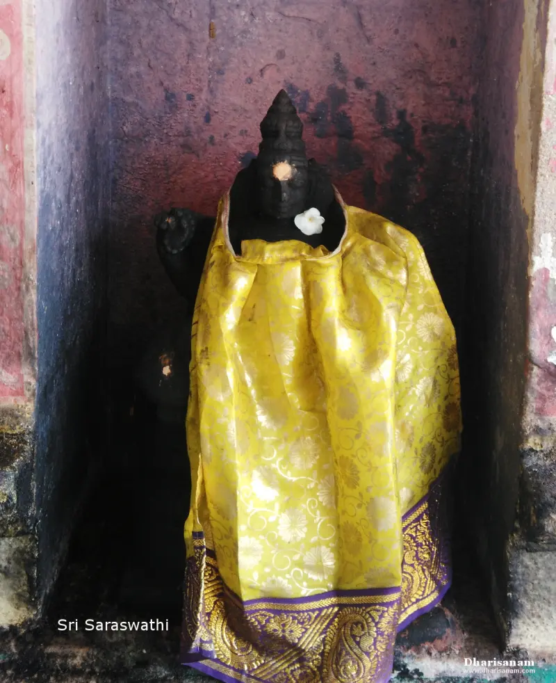 A dark stone idol in a niche, dressed in a yellow silk cloth with a white flower at the neck