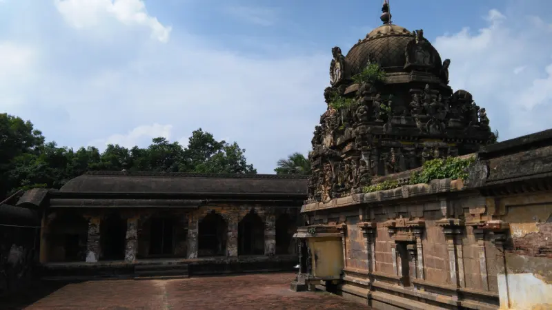 A dark stone domed shrine tower with carved figures, and a long pillared corridor across a brick courtyard.