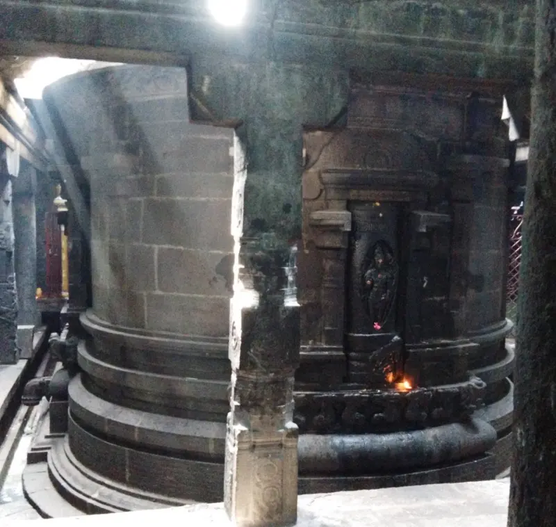 Curved stone walls of the sanctum, with a small carved figure in a niche and a lamp burning below.