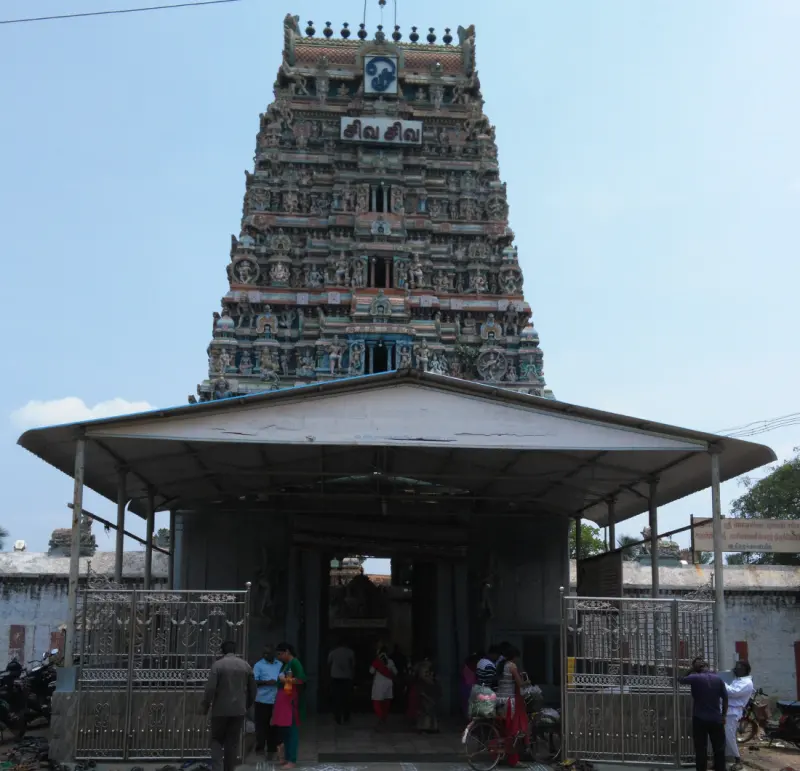 A tiered gateway tower with painted figures above an entrance with a canopy, iron gates and visitors outside.