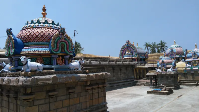 Painted domes with white bulls above a stone wall; more shrines and an arched roof stand further along