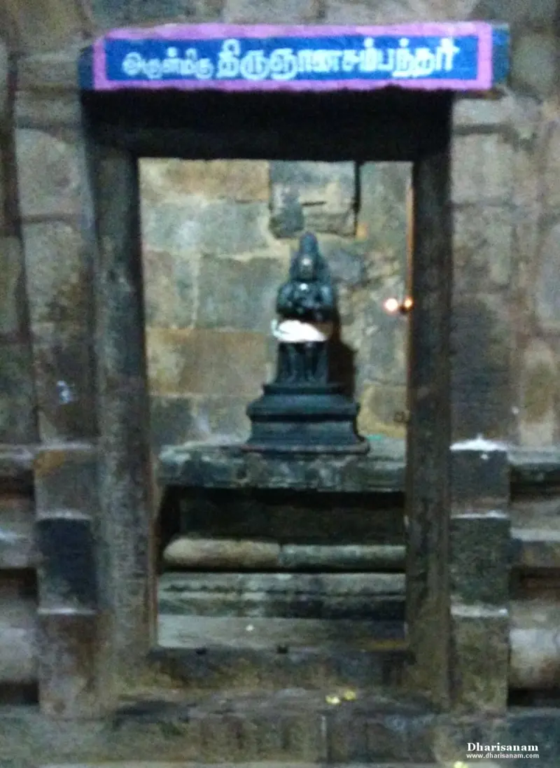 A small dark idol in a stone niche under a blue Tamil name board