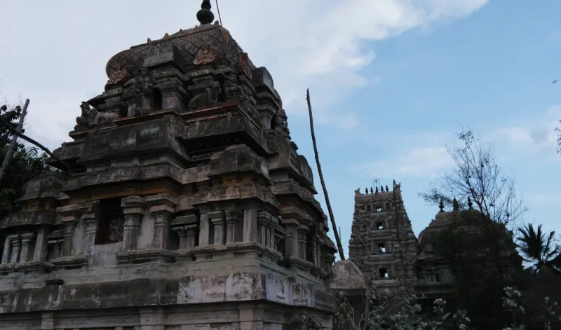 A weathered stone vimana with a domed top, and the gopuram visible to its right