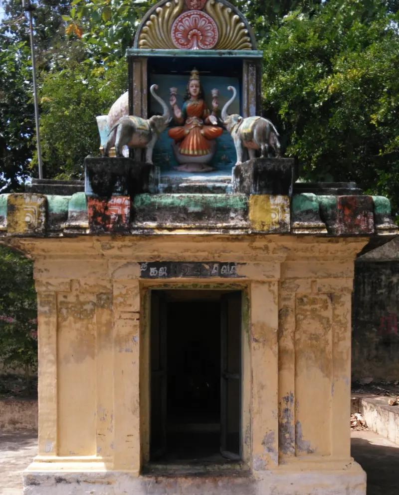 A small weathered shrine with a seated Lakshmi figure flanked by two elephants above a dark doorway.