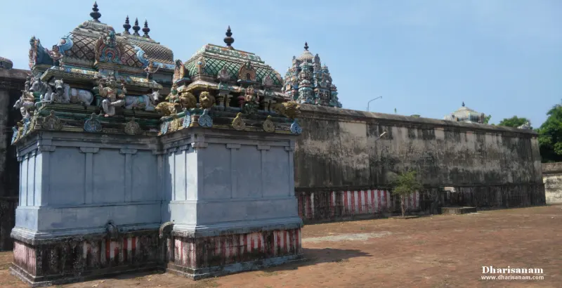 Two grey shrines with carved, painted domes beside a long wall with red and white stripes