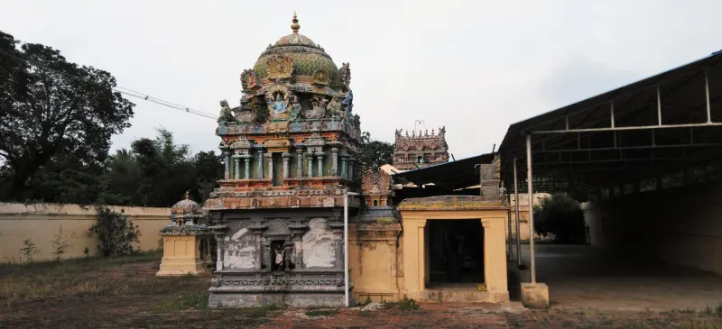 A coloured domed shrine tower in a courtyard beside a small shrine and a long tin-roofed shed.