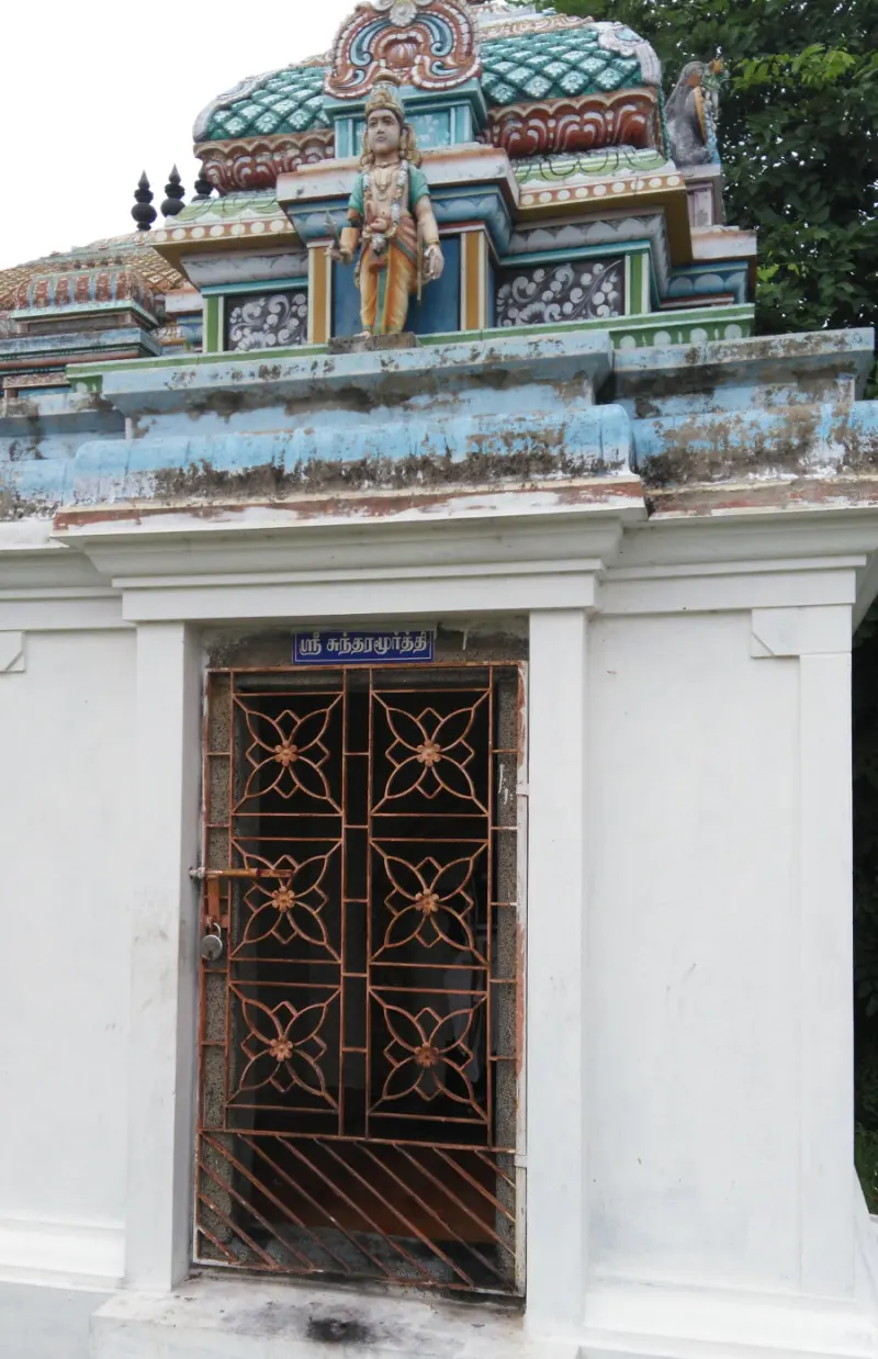 A white shrine with an ornate iron gate, and a standing painted figure above the doorway.
