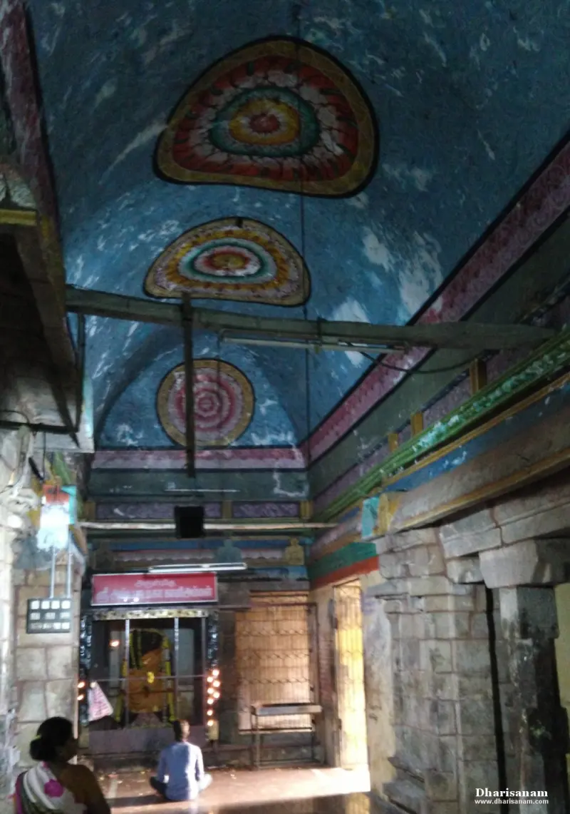 A blue vaulted ceiling painted with large round floral designs, and a lit shrine with a seated devotee below