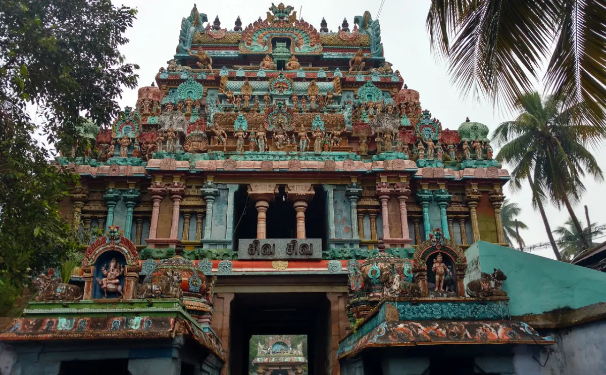 A tall tower of many painted tiers above a dark entrance passage, with palm trees beside it.
