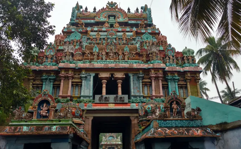 A tall tower of many painted tiers above a dark entrance passage, with palm trees beside it.