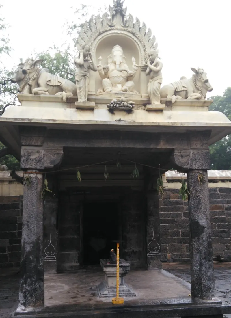 A shrine with a white stucco Ganesha under an arch, flanked by two bulls and two small figures, over a stone pedestal.