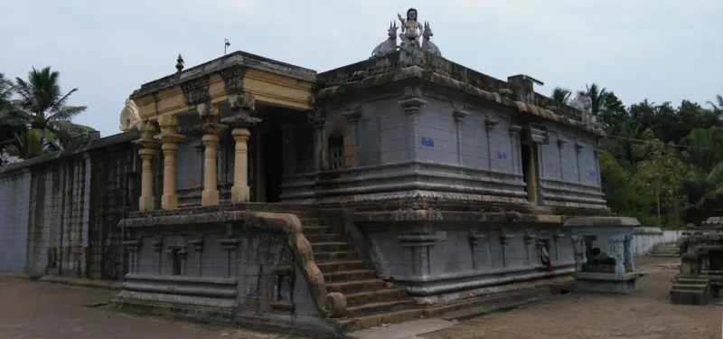 A grey stone temple on a raised base, a pillared porch at the left and a flight of steps to the sanctum.